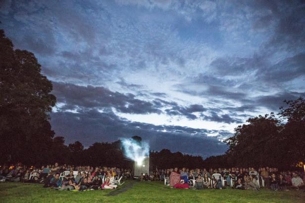 Eine Menschenmenge sitzt im Freien und schaut einen Film auf einer Leinwand.