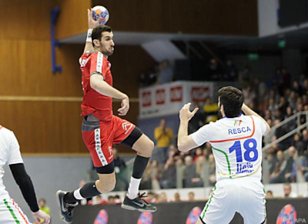 Ein Handballspieler in rotem Trikot springt, um den Ball zu werfen.