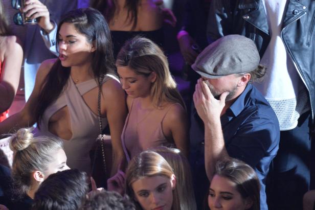 Leonardo DiCaprio mit einer Schiebermütze umgeben von mehreren jungen Frauen.