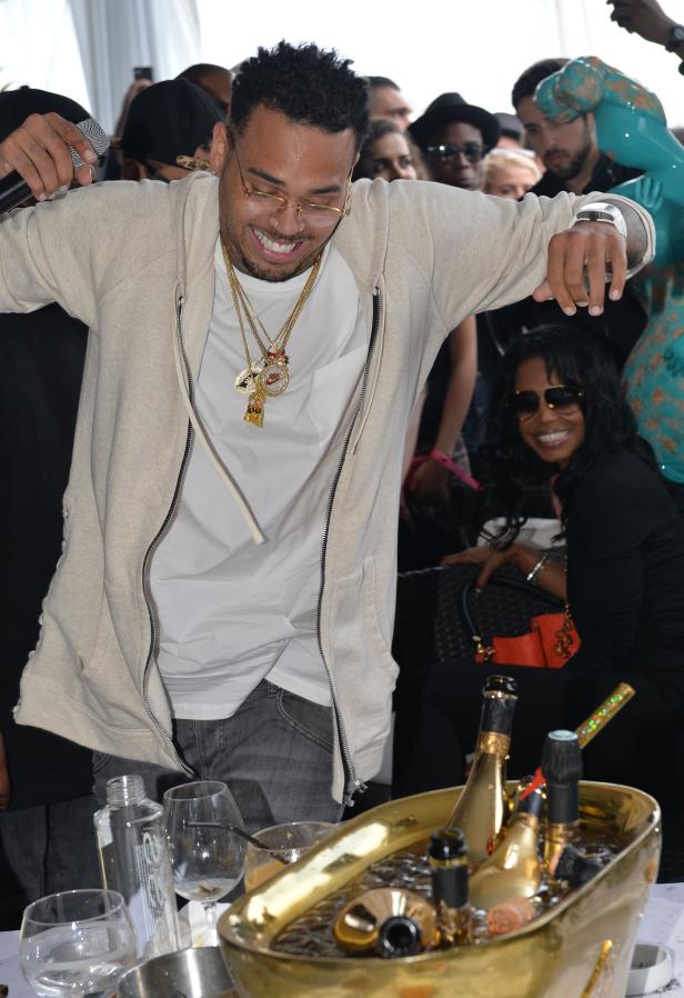 Chris Brown hält ein Mikrofon in der Hand, umgeben von Menschen und Champagner.