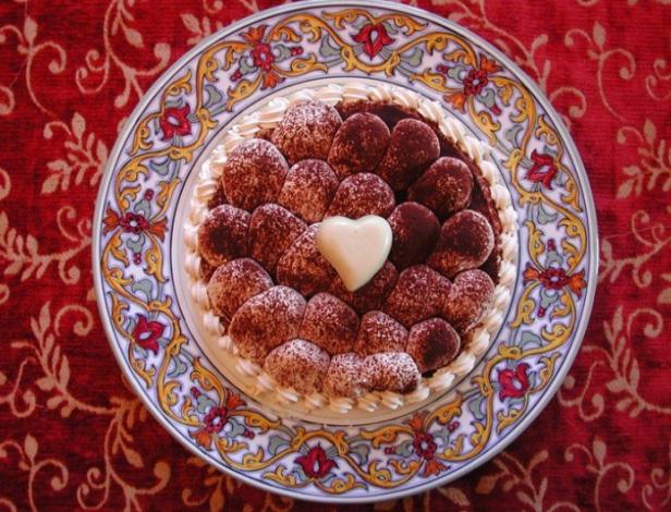 Ein Tiramisu-Kuchen mit Schokoladenkugeln und einem weißen Schokoladenherz auf einem verzierten Teller.