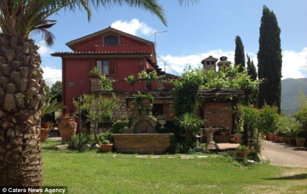 Ein rotes Haus mit einem Garten und einem Brunnen im Vordergrund.
