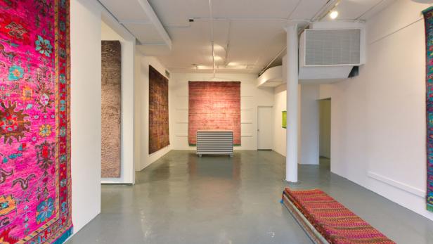 Ein Ausstellungsraum mit verschiedenen Teppichen an den Wänden und auf dem Boden.