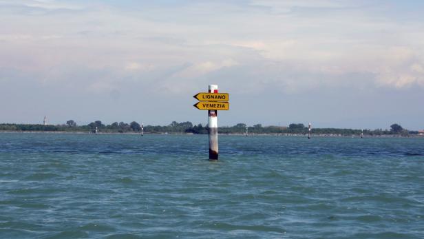 Ein Wegweiser im Wasser zeigt in Richtung Lignano und Venedig.