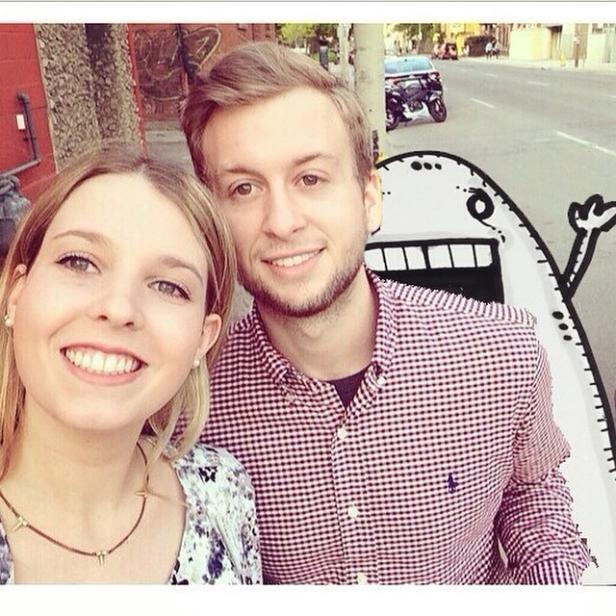 Ein junges Paar macht ein Selfie auf der Straße, im Hintergrund ein gekritzeltes Monster.