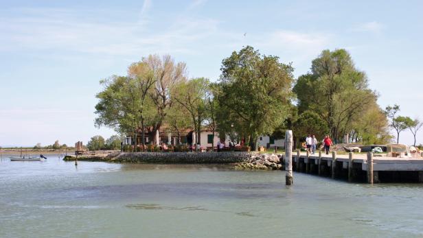 Ein Restaurant am Wasser mit Gästen und ein Steg mit Passanten.