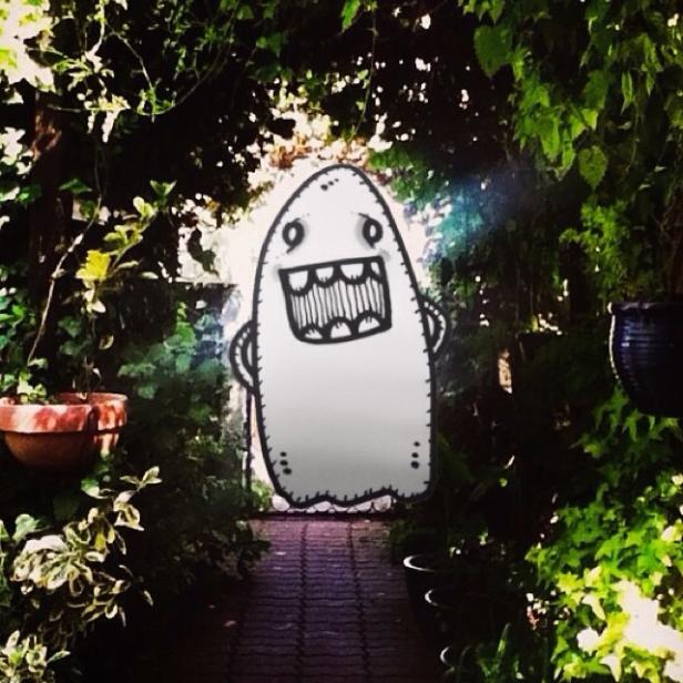 Ein gezeichnetes, grinsendes Gespenst steht in einem grünen Garten.