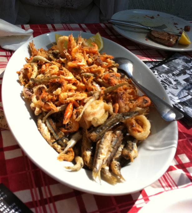 Eine Platte mit frittierten Meeresfrüchten, darunter Garnelen und kleine Fische, garniert mit Zitrone.