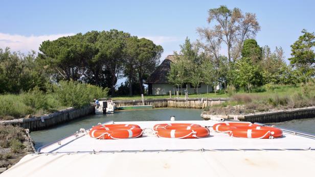 Blick von einem Boot auf einen Kanal mit einem Haus mit Strohdach im Hintergrund.