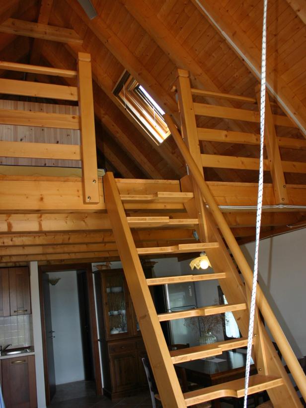 Eine Holztreppe führt zu einem Zwischengeschoss in einem Zimmer mit Holzbalkendecke.