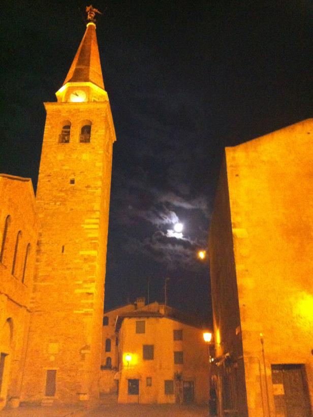 Ein beleuchteter Kirchturm und Gebäude unter einem Nachthimmel mit Mond.