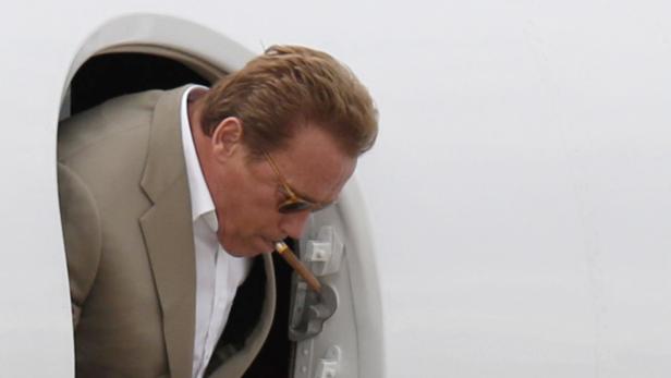 Arnold Schwarzenegger steigt mit einer Zigarre im Mund aus einem Flugzeug.