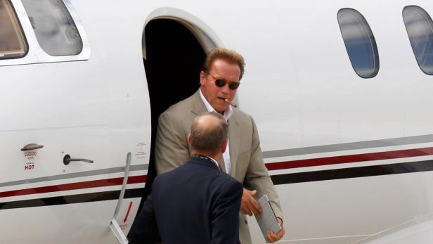 Arnold Schwarzenegger verlässt mit Zigarre und Sonnenbrille ein Flugzeug.