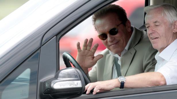 Arnold Schwarzenegger winkt aus dem Fenster eines Autos.
