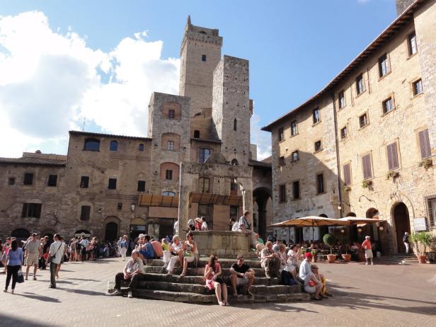 Menschen sitzen und gehen auf einem Platz in San Gimignano, Italien.