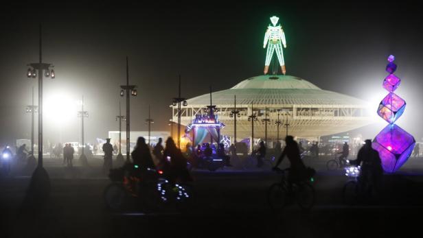 Nachts in der Wüste Nevada: Menschen und Fahrräder vor dem beleuchteten „Burning Man“.