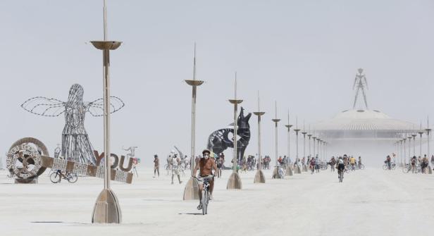 Besucher fahren mit Fahrrädern durch die staubige Landschaft des Burning Man Festivals.