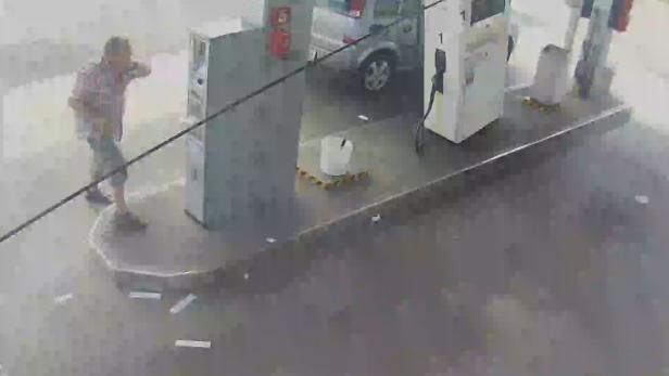 Ein Mann steht an einer Tankstelle und telefoniert.