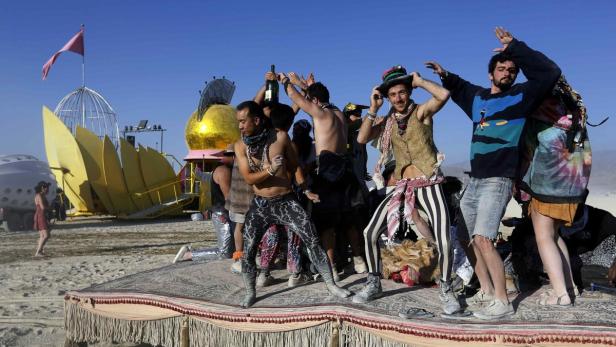 Eine Gruppe von Menschen tanzt auf einem dekorierten Teppich in der Wüste, möglicherweise auf dem Burning Man Festival.