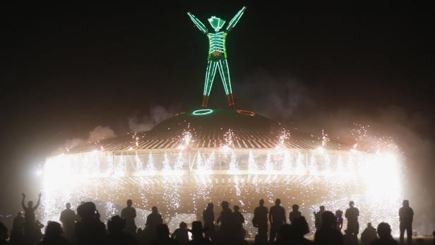 Eine Menschenmenge beobachtet das Burning Man Festival mit einer beleuchteten Figur und Feuerwerk.