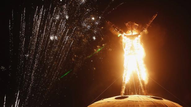 Beim Burning Man Festival steht eine riesige, brennende Statue vor einem Feuerwerk.