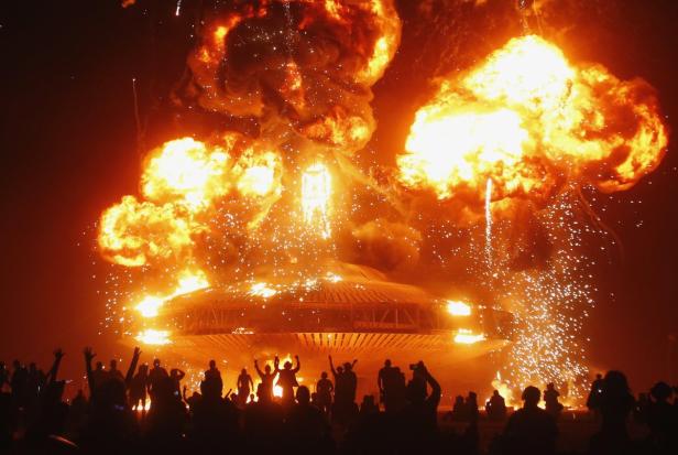 Eine Menschenmenge beobachtet, wie ein großes, rundes Gebäude in einer Feuer- und Funkenexplosion zerstört wird.