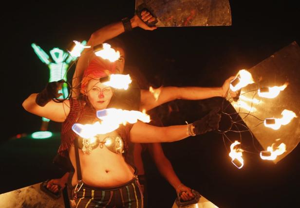 Eine Frau mit roter Nase und Kopfbedeckung führt eine Feuershow auf.