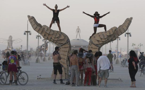 Zwei Frauen posieren auf einer großen, hölzernen Handskulptur auf dem Burning Man Festival.