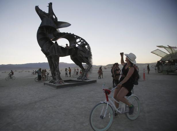Eine Frau auf einem Fahrrad fotografiert eine große Wolfsskulptur in der Wüste.