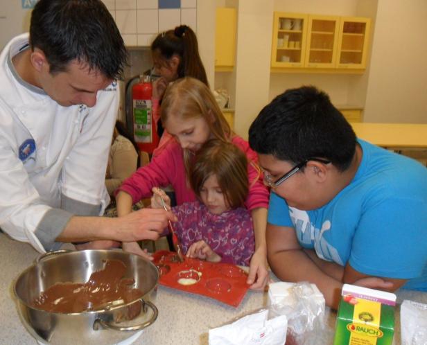 Ein Koch und drei Kinder füllen Schokoladenformen.