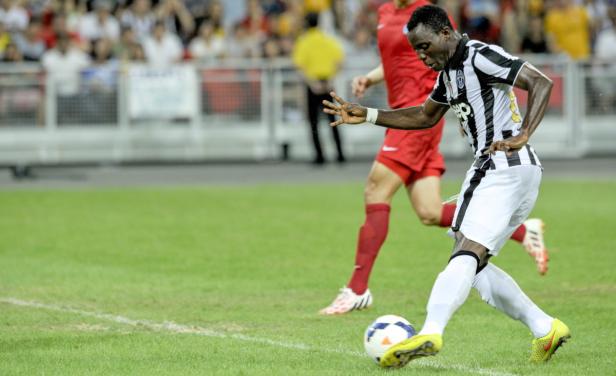 Ein Fußballspieler in einem schwarz-weiß gestreiften Trikot schießt einen Ball.