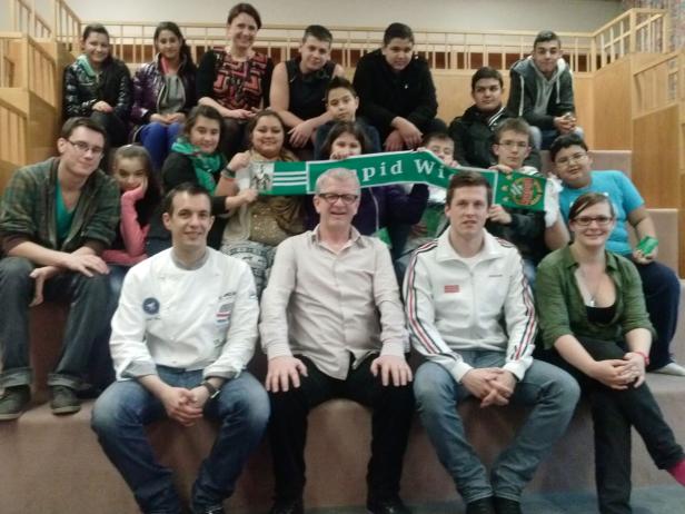 Eine Gruppe von Menschen sitzt auf einer Treppe und hält einen „Rapid Wien“-Schal.