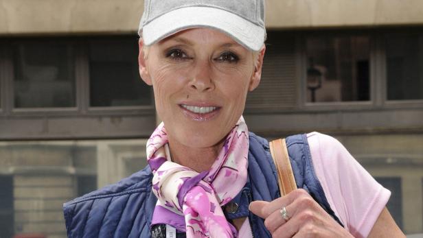 Eine Frau mit Kappe, Weste und Tuch lächelt in die Kamera.