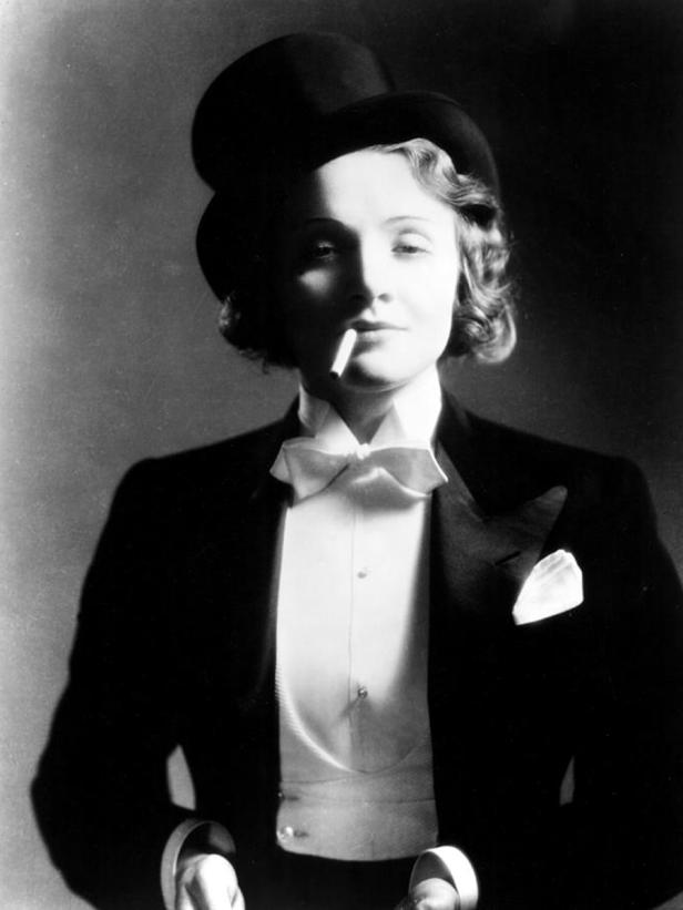Marlene Dietrich im Smoking mit Zylinder und Zigarette im Mundwinkel.