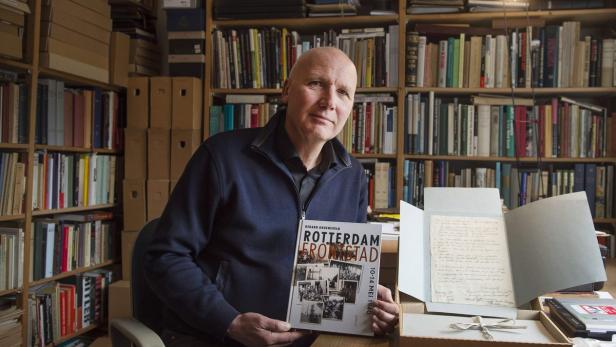 Ein Mann präsentiert das Buch „Rotterdam Brandstad 10-14 Mei 1940“ vor einem Bücherregal.