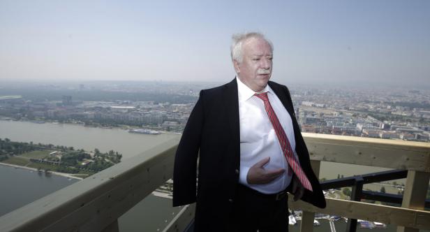 Ein Mann im Anzug steht auf einer Aussichtsplattform mit Blick auf eine Stadt.