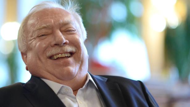 Ein älterer Mann mit Schnurrbart lacht herzlich.