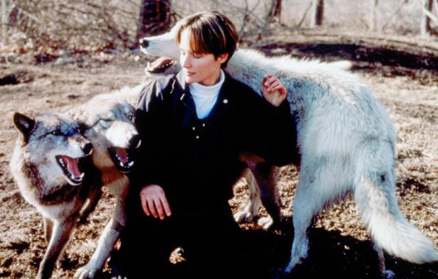 Eine Frau kniet inmitten von drei Wölfen in einer Waldlichtung.