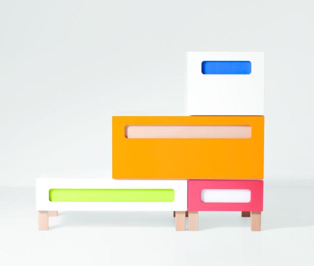 Ein gestapeltes, farbenfrohes Regal mit Schubladen in Weiß, Orange, Pink und Grün steht im Raum.