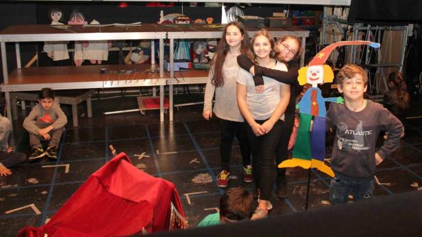 Eine Gruppe von Kindern steht auf einer Bühne mit einer bunten Clown-Puppe.