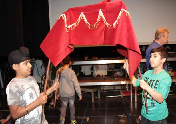 Zwei Jungen halten ein rotes Tuch mit Fransen auf einer Bühne.