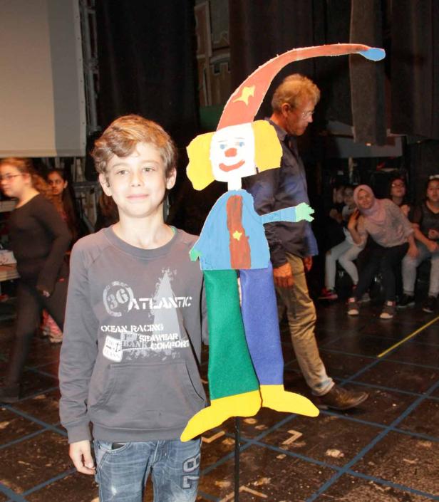 Ein Junge steht mit einer selbstgemachten Clown-Puppe auf einer Bühne.