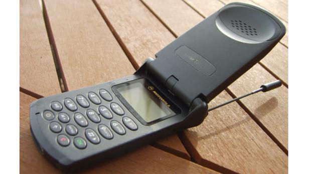 Ein geöffnetes Motorola StarTAC Klapphandy liegt auf einem Holztisch.