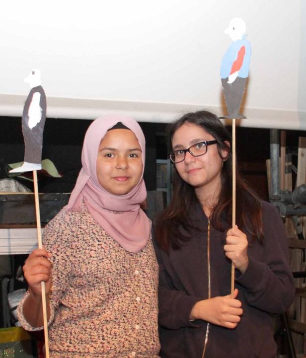 Zwei junge Frauen halten selbstgebastelte Figuren an Stöcken hoch.