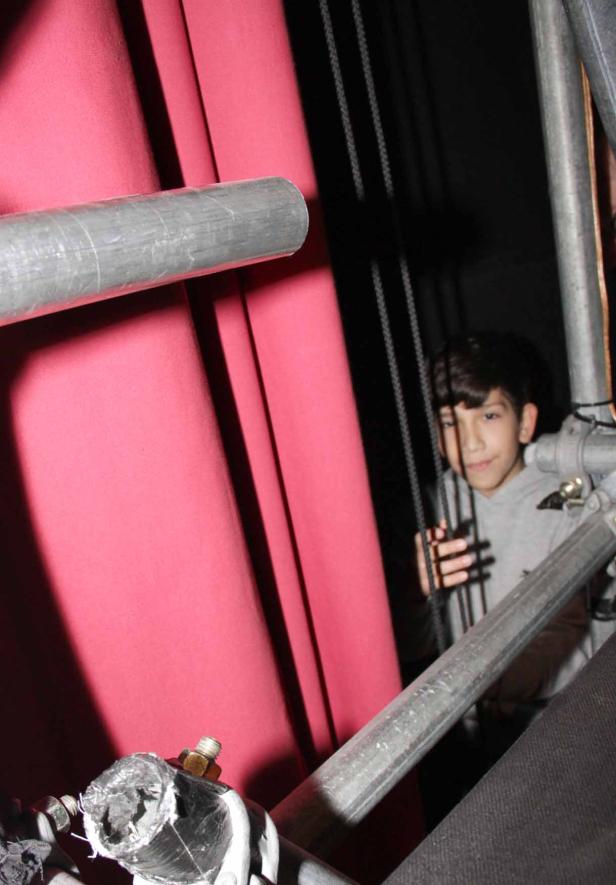 Ein Junge schaut hinter einer Bühnenkonstruktion hervor.