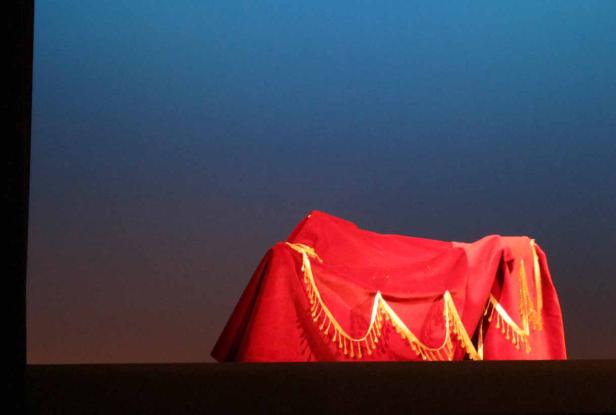 Ein mit einem roten Tuch mit goldenen Verzierungen verdeckter Gegenstand auf einer Bühne.