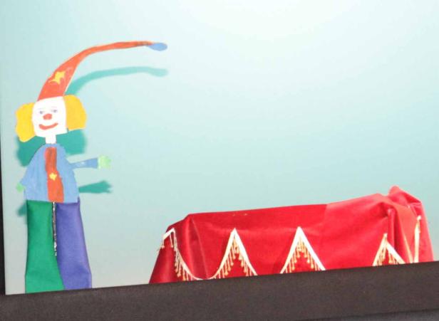 Eine Kinderzeichnung zeigt einen Clown neben einem mit rotem Samt bedeckten Tisch.
