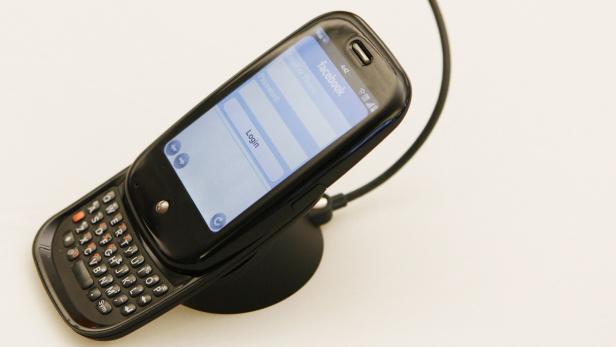 Ein Slider-Handy mit QWERTZ-Tastatur zeigt den Facebook-Login-Bildschirm.