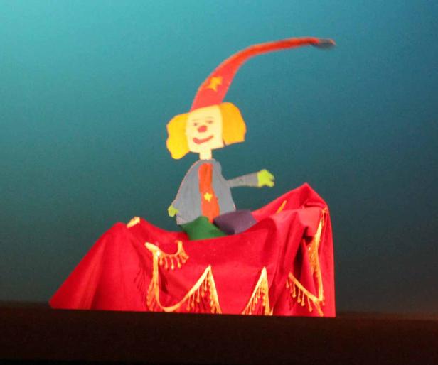 Eine Marionette mit Clown-Gesicht und rotem Hut auf einer Bühne.