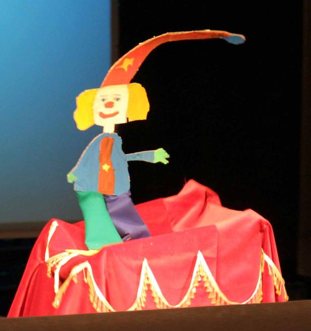 Eine handgemachte Clown-Marionette steht auf einer roten Bühne.